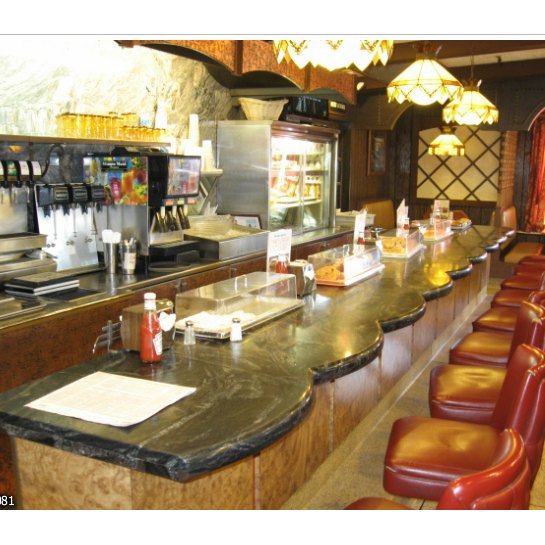 The counter at Twin Pines Diner, with red stools, a dark stone countertop and a dessert case