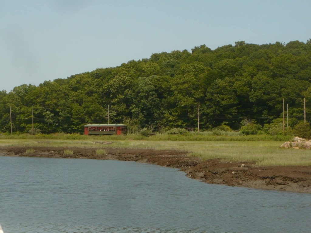 A yellow trolley crosses the marsh along the Farm River at the Shore Line Trolley Museum