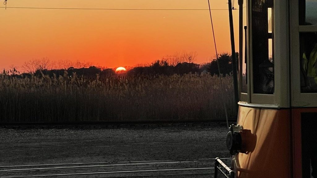The sun sets over the salt marsh beside a vintage trolley on the Branford Electric Railway