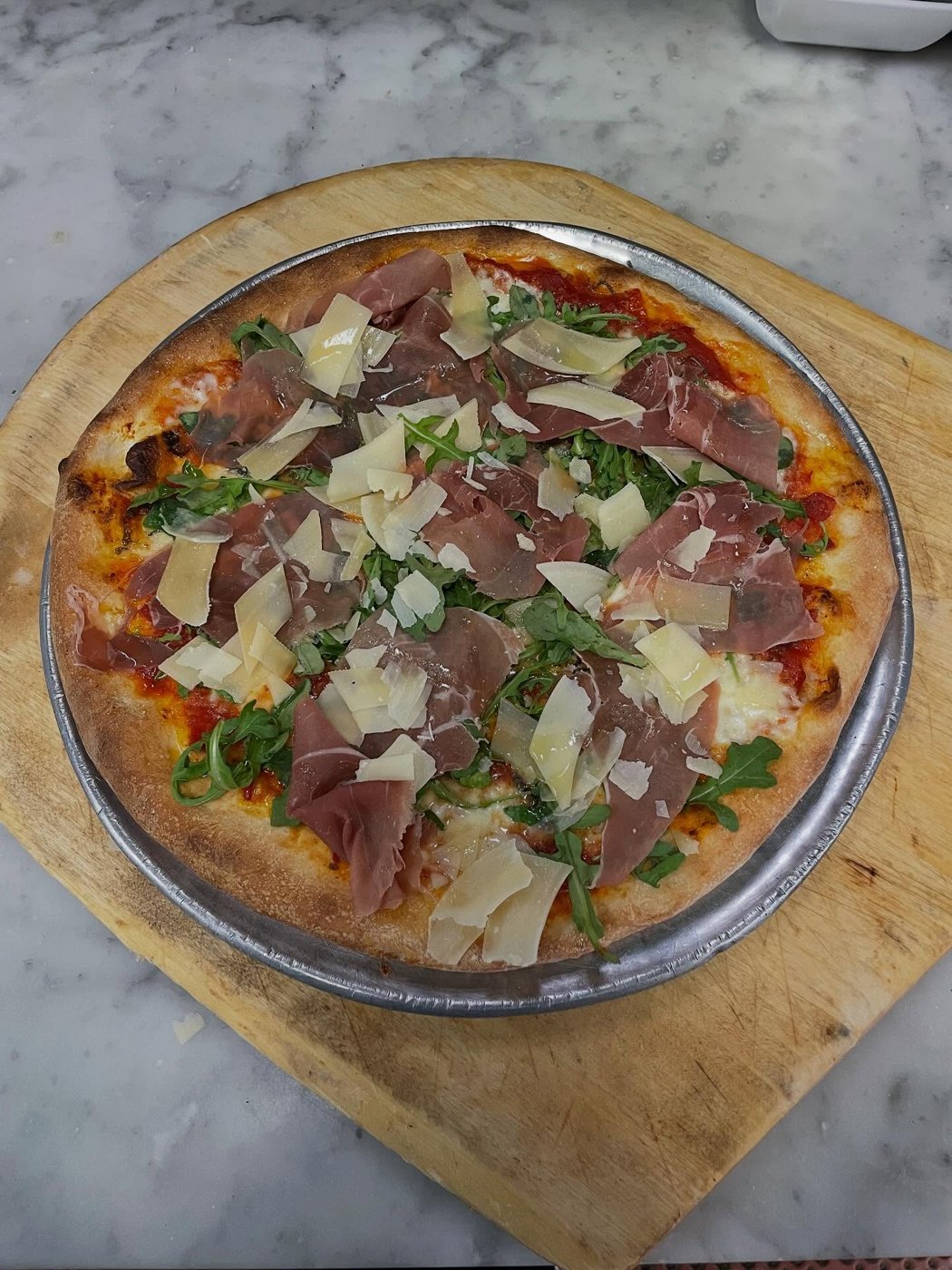 A round pizza topped with prosciutto and shaved cheese at Aniello's